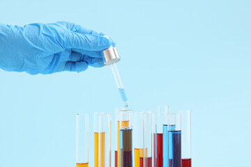 Lab's worker hand with pipette dripping samples into test tubes on blue background