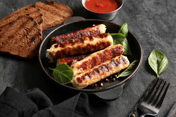 Frying pan of tasty grilled sausages on black background