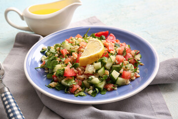 Plate with delicious tabbouleh salad and oil on light background, closeup