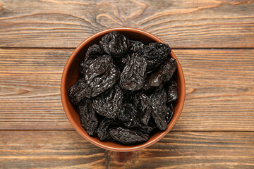 Bowl with tasty dried plums on wooden background