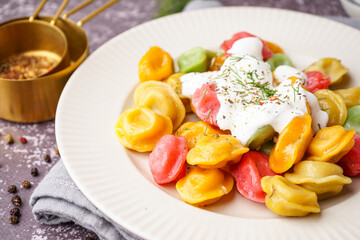Plate of boiled colorful dumplings with sour cream and dill on dark background
