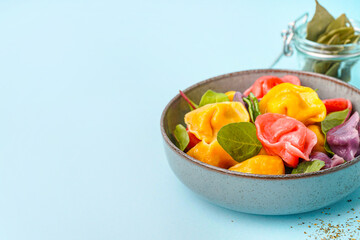 Bowl with boiled colorful dumplings and spinach on blue background