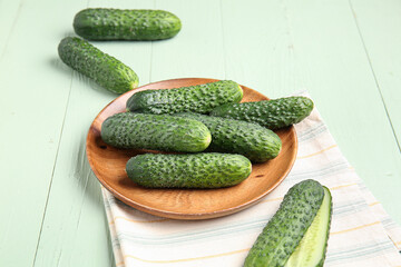 Plate with fresh cucumbers on green wooden background