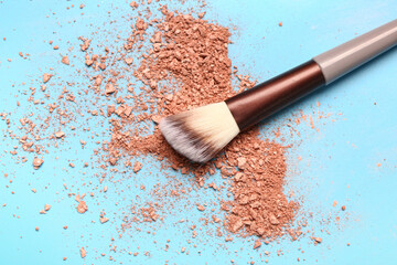 Makeup brush and scattered highlighter on blue background