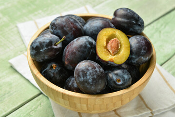 Bowl with fresh plums on green wooden background