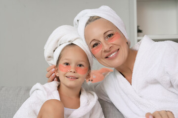 Little girl and her grandmother with under-eye patches at home, closeup