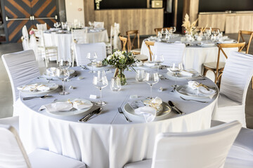 A wedding table covered with a white tablecloth, decorated with flowers, candles, glasses and cutlery.