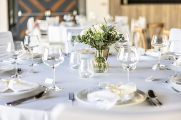 A wedding table covered with a white tablecloth, decorated with flowers, candles, glasses and cutlery.
