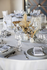 A wedding table covered with a white tablecloth, decorated with flowers, candles, glasses and cutlery.