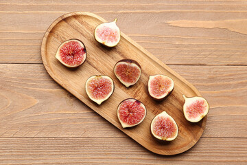 Board with halves of fresh ripe figs on wooden background