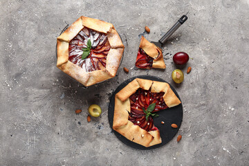 Stand and board of delicious plum galette with mint on grey background
