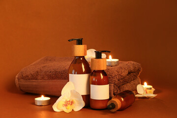 Bottles of cosmetic products, clean towel and burning candles on color background
