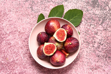 Plate with ripe fresh figs and plant leaves on grunge pink background