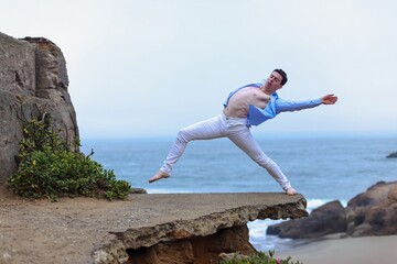 Male ballet dancer perfromance artist on the beach balancing on a concrete structure
