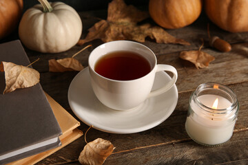 Cup of tea with books, autumn leaves and burning candle on wooden background