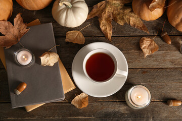 Cup of tea, books, autumn leaves, burning candles and pumpkins on wooden background