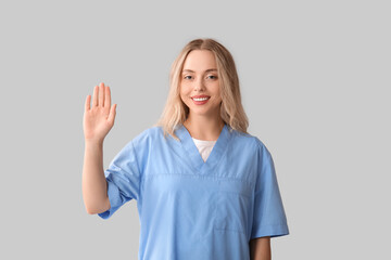 Fototapeta premium Beautiful female doctor waving hand on grey background