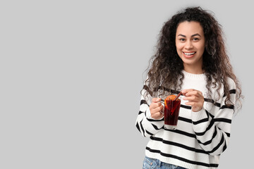 Beautiful young African-American woman with glass cup of hot mulled wine on grey background