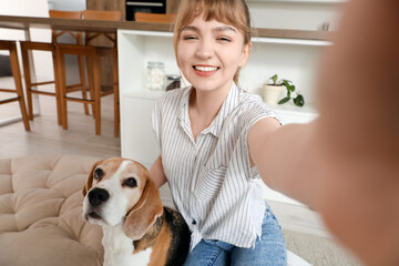 Young woman with cute beagle dog taking selfie at home