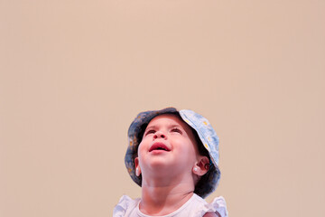 A child wearing a blue and white bucket hat with yellow polka dots, a sleeveless ruffled white top,...