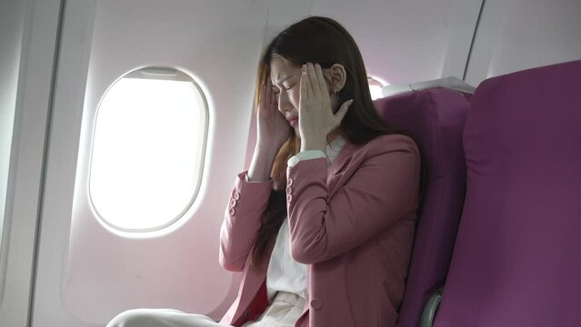 A young Asian woman is sitting in her seat as an airplane passenger, experiencing airsickness with symptoms like nausea, vomiting, dizziness, and general discomfort.