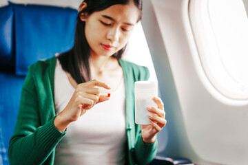 A young Asian woman is sitting in her seat as an airplane passenger, experiencing airsickness with...