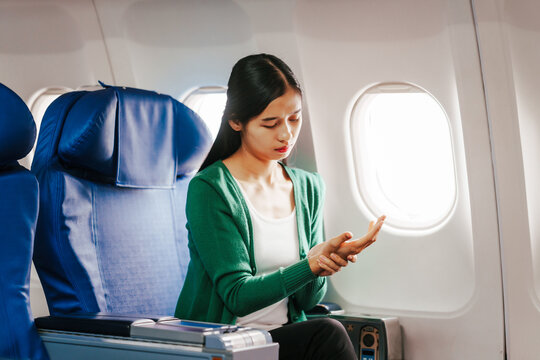 A young Asian woman is sitting in her seat as an airplane passenger, experiencing airsickness with symptoms like nausea, vomiting, dizziness, and general discomfort.