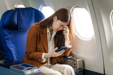 A young Asian woman is sitting in her seat as an airplane passenger, experiencing airsickness with...