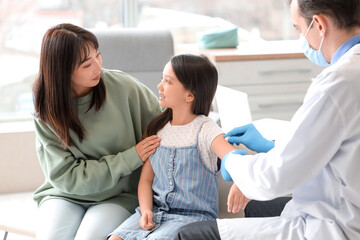 Fototapeta premium Little Asian girl with her mother receiving vaccine in clinic