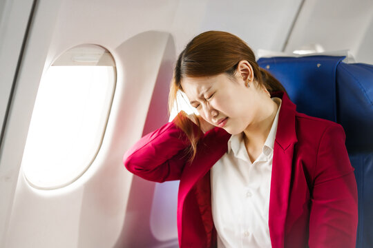 A young Asian woman is sitting in her seat as an airplane passenger, experiencing airsickness with symptoms like nausea, vomiting, dizziness, and general discomfort.