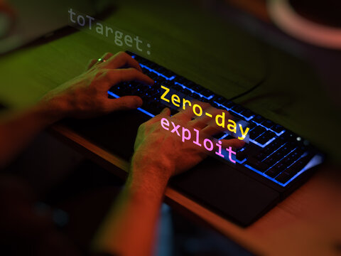 Cyber attack zero-day exploit text in foreground screen, hands of a anonymous hacker on a led keyboard. Vulnerability text in informatic system style, code on editor screen.