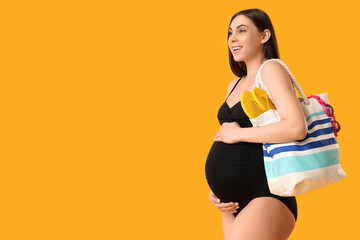 Young pregnant woman in swimsuit holding bag on yellow background. Travel concept