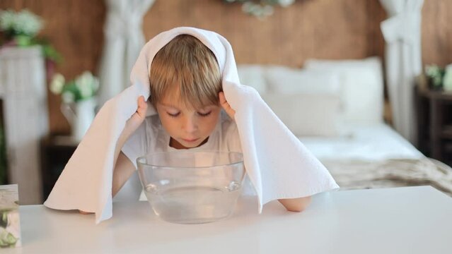 School boy, child, doing steam inhalation at home to soothe and open nasal passages, alternative method of heailing runny nose