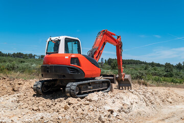 Obraz premium Escavadora de esteiras a trabalhar em terreno montanhoso para a construção de uma estrada sob um céu limpo e cercada por paisagens naturais