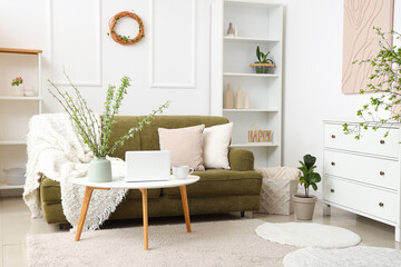 Green sofa, coffee table and vase with blossoming branches in light living room