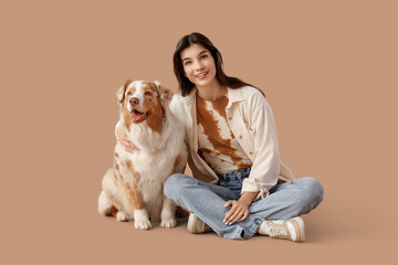 Young woman with Australian Shepherd dog sitting on beige background