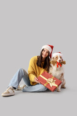 Young woman with Australian Shepherd dog in Santa hats and Christmas gifts on light background