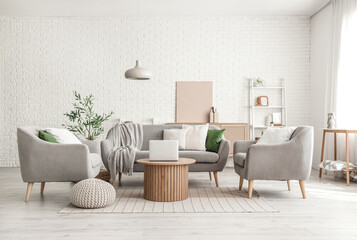 Stylish interior of living room with cozy sofa, armchairs, coffee table, laptop and olive tree