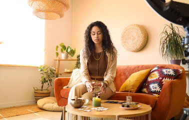Young African-American witch with crystal ball recording video at home