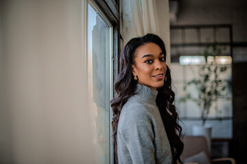 Close-up portrait of a young african-american woman standing at the window and looking at camera