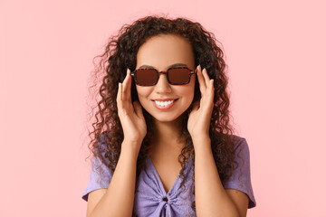 Happy young African-American woman in sunglasses on pink background