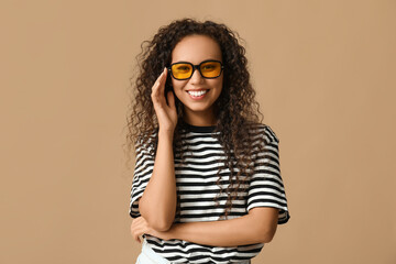 Happy young African-American woman in sunglasses on beige background