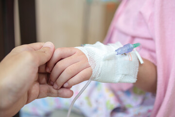 Mother holding child hand with saline IV solution in hospital