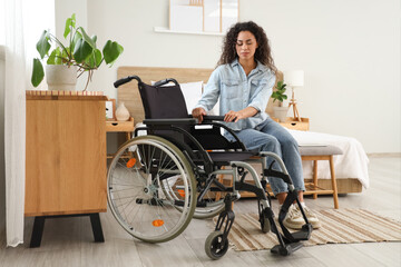 Young African-American woman with wheelchair sitting on bench at home