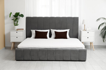 New orthopedic mattress on stylish bed near window in room