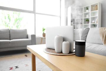 Air humidifier with vases and laptop on table in living room, closeup
