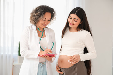 Female doctor writing prescription for young pregnant woman in clinic