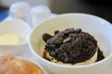 A dessert of cookies and cream cheesecake with raspberry coulis, with fresh bread roll and pat of butter served on a business class flight from Sydney, Australia to Kuala Lumpur, Malaysia