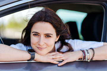 Happy woman looking at camera from car window and smiling while relaxing