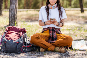 Young woman holding smartphone and checking gps while relaxing in the forest after hiking